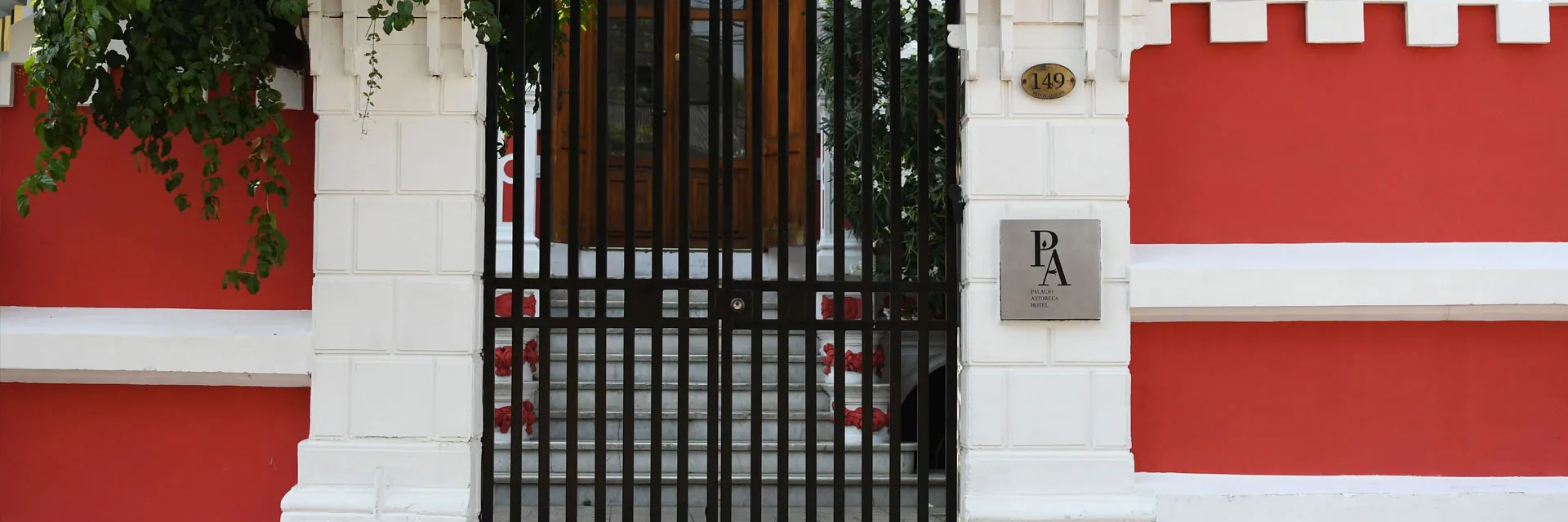 Fachada roja y blanca del Palacio Astoreca detrás de su reja de entrada
