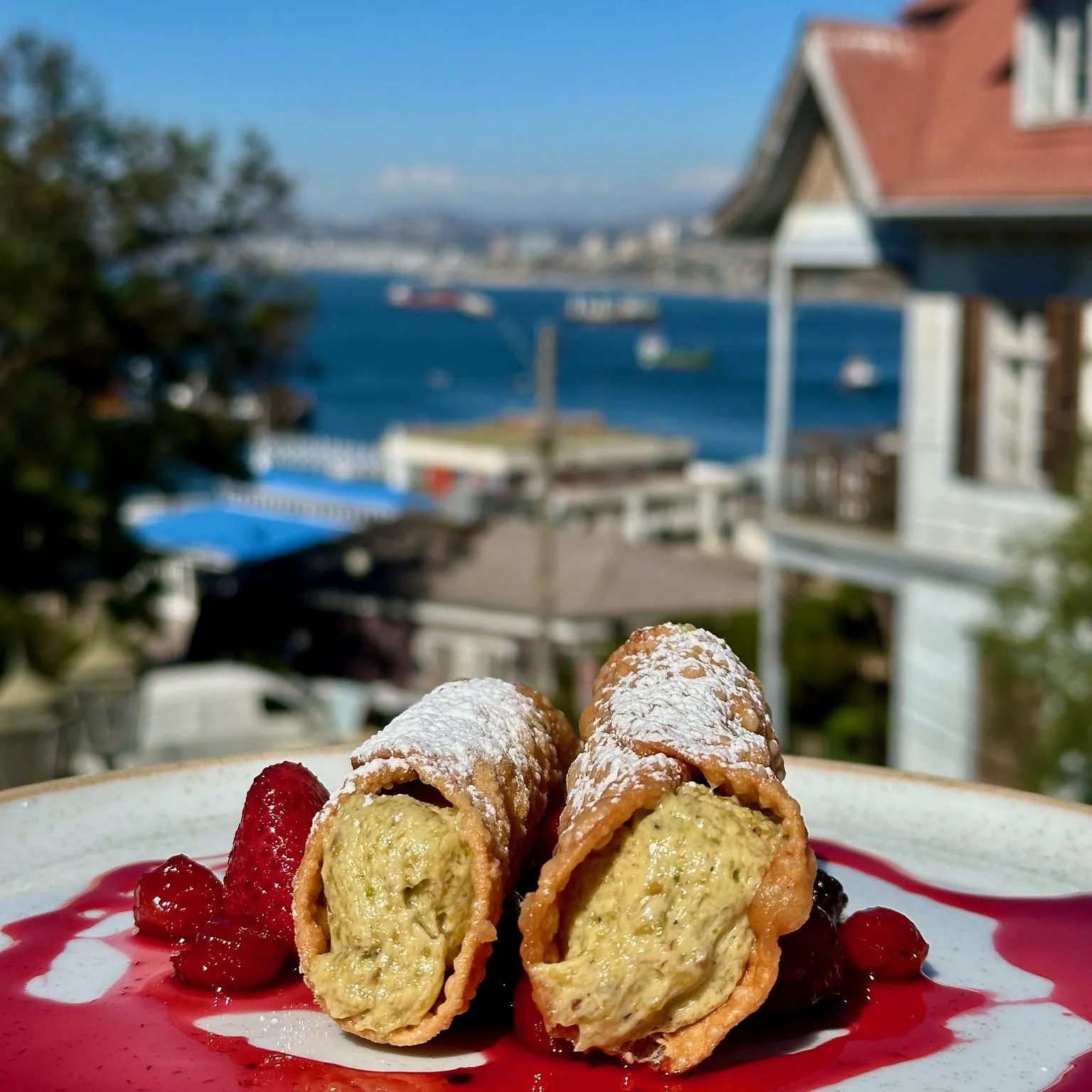 Cannoli sobre una mesa de Pastalegre con la bahía de Valparaíso al fondo